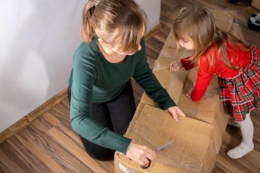 Anne elinde makasla elinde küçük kızıyla, içinde Noel ağacı olan karton kutuyu açıyor.. 