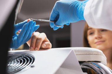 Kozmetik uzmanı kadın manikürcü. Küçük bir makasla tırnaklarını kesiyor. Güzellik salonunda tırnaklarını nazikçe kesiyor..