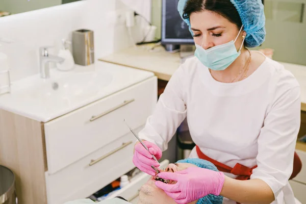 Dentist in a medical mask and pink protective gloves working using dental instruments with man teeth in dental clinic. — Stockfoto
