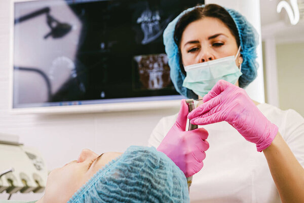 Закрыть фотографию врача-стоматолога в униформе, готовящего стоматологическое оборудование для начала работы с пациентом в ее офисной клинике.