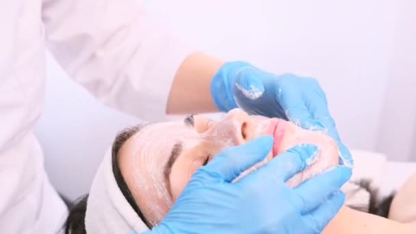 ศัลยแพทย์ใช้ครีมให้ความชุ่มชื้นบนใบหน้าของผู้หญิงที่สวยงามและนวดโดยใช้มือในถุงมือ . — วีดีโอสต็อก