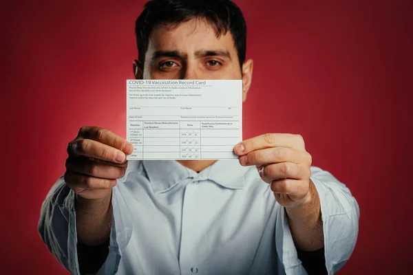 Tired doctor holding coronavirus vaccination record card, isolated on red background. — Φωτογραφία Αρχείου