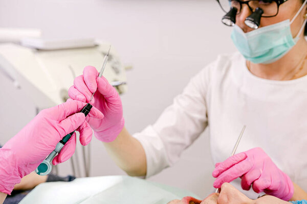 Dentists in uniform and with medical equipment are working in modern stomatology clinic together with an assistant.