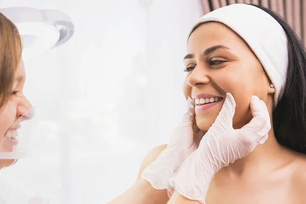 Hübsche Frau mit breitem Lächeln erhält von Kosmetikerin Inspektion des Gesichts im Medical Center Klinik Kursalon. — Stockfoto