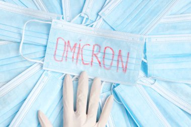 Covid 19 virüsünün bir çeşidi olan Omicron, birçok maskeyle çevrili bir eldiven içindeki bir eldiven ile tıbbi bir maskeye yazılmıştır..