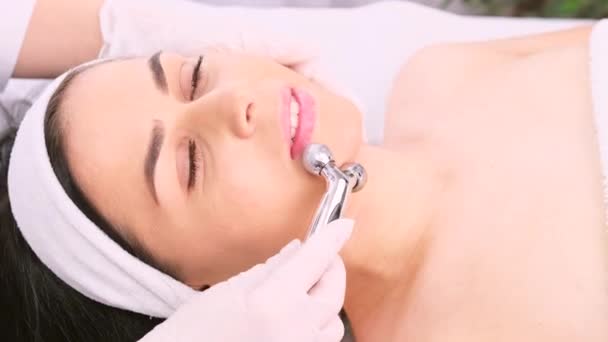 Detailní video krásné ženy s ručníkem na hlavě dostat masáž obličeje Y-tvarovaný míč váleček v salonu krásy. — Stock video