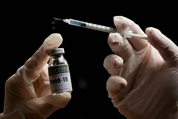 Fotografía de cerca de las manos del médico sosteniendo un vial de vacuna para la inmunización y una jeringa con un líquido con gotas de inyección. — Foto de Stock