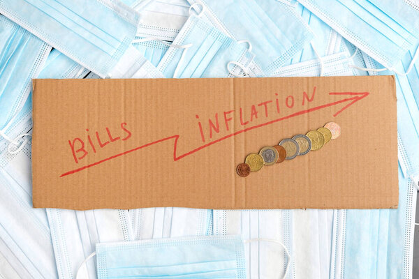 Закрыть фотографию картона со стрелкой вверх знак и монеты с большим количеством медицинских масок, оплата счетов проблема в пандемии концепции.