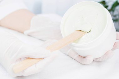 Kozmetik uzmanının elinde bir kavanoz krem ürün kıracağı tutan tıbbi eldivenlerle kozmetolog dolabındaki kavanozdan çıkarmaya çalışırken çekilmiş bir fotoğrafı..