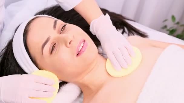 Mladá žena podstupující omlazovací tělový zákrok kosmetičkou pomocí dvou houbiček na kosmetické klinice. — Stock video