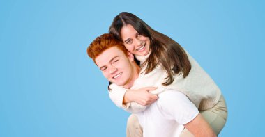 Birbirine aşık iki genç kız eğleniyor, oldukça neşeli, sevimli, gülümseyen bir kız, mavi arka planda yalnız bir şekilde erkek arkadaşlarının üzerinde oturuyor..