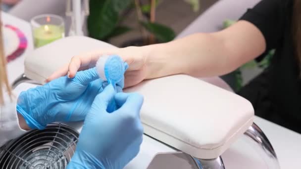 Close-up video van een manicure handen in blauw handschoenen borstelen een nagel voor het schilderen van klanten nagels met polish in schoonheidssalon. — Stockvideo