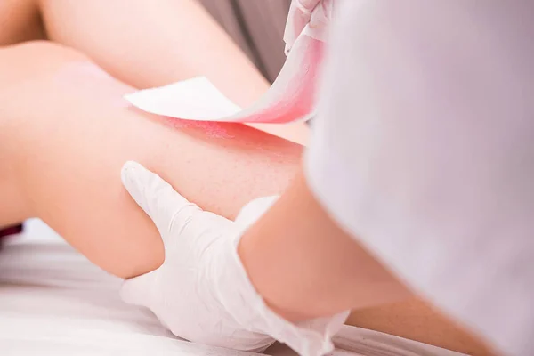 Woman with long tanned perfect legs and smooth skin having wax stripe depilation hair removal procedure on legs in beauty salon. — Stock Photo, Image
