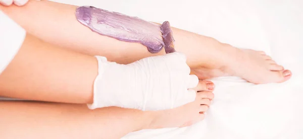 Cosmetologo in guanti bianchi applica cera calda con spatola a una gamba di donna per fare procedura di depilazione su gambe in salone di bellezza. — Foto Stock