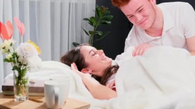 Sevgilisi, sevgililer gününde yatak odasında kadehte çiçeklerle ve masada bir bardakla uyanır ve birlikte güler..