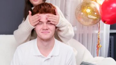 Sıcak süveter giyen genç bir kız arkasında kızıl saçlı ve balonlu sevgilisine gözlerini kapatıyor..