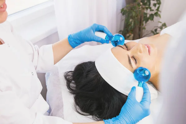 Kosmetikerin mit Gesichtsroller zu einer Patientin mit weißem Verbandtuch auf der Stirn in einem Schönheitssalon. — Stockfoto