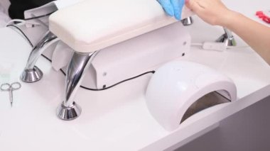 Profesyonel uzman, mavi eldivenli. Kadın müşteriye, tırnaklarını ojeyle ovalaması gereken ekipmanları gösteriyor..