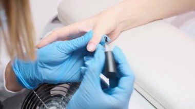 Mavi eldivenli manikür ustası bir güzellik salonunda tırnaklarına oje sürüyor, manikür konseptini hallediyor..