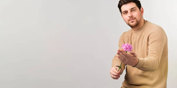 Ung stilig man bär tröja med vacker blomma innehav i handen står över vit bakgrund. — Stockfoto