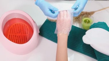  Kozmetik uzmanı, parafin banyosundan sonra güzellik salonundaki eller için müşteri ellerine parafin eldivenleri takıyor..