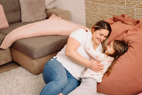 Alegre familia de dos personas madre y encantadora niña acostada en una gran almohada junto con una manta en el sofá. — Foto de Stock