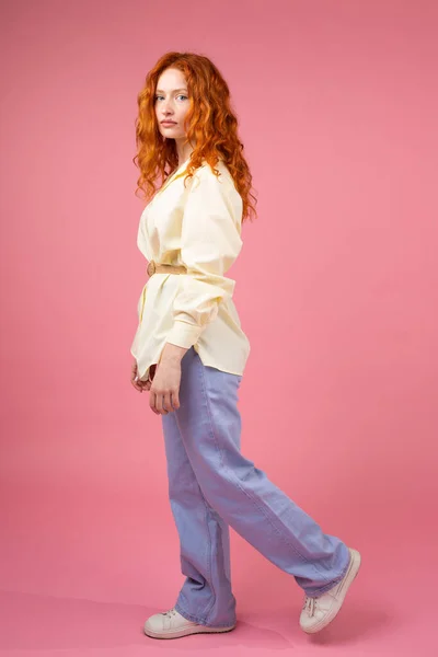 Pleine longueur vue de côté photo d'une fille sérieuse à venir belle en vêtements modernes regardant l'appareil photo sur fond rose, beau concept de coiffure. — Photo