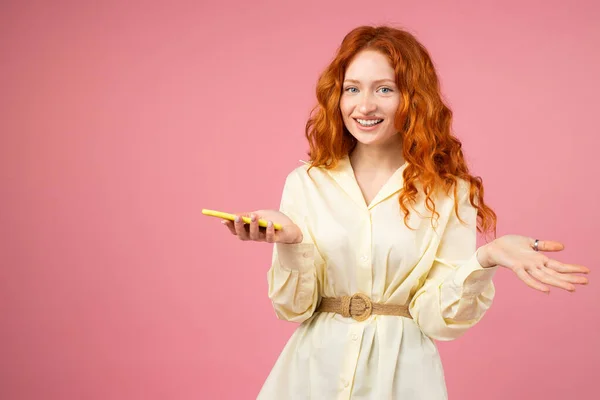Genç, inanılmaz kızıl saçlı kadın bir elinde akıllı telefonu tutuyor ve pembe arka planda fotokopi aletiyle gülümsüyor..
