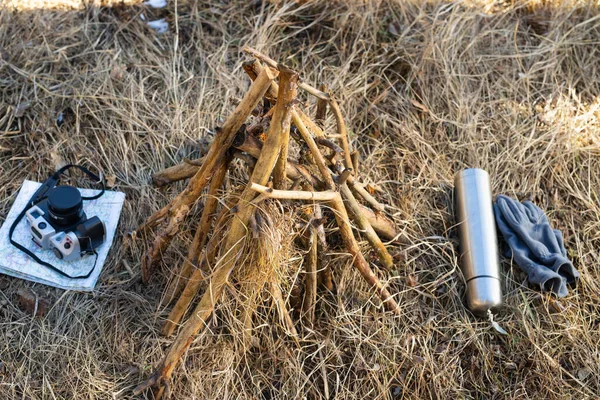 Närbild foto av en brasa utomhus i skogen med en kamera och karta också en termos flaska med handskar nära brasan. — Stockfoto