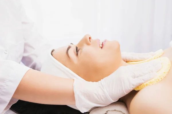 Cosmetologa professionista femminile che utilizza spugne per pulire il collo di una cliente donna che si prepara per una procedura di ringiovanimento cosmetico. — Foto Stock