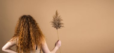 Kızıl saçlı, uzun kıvırcık saçlı, bir elinde kamış dalıyla altın arka planda poz veren bir kadının arka plan fotoğrafı..