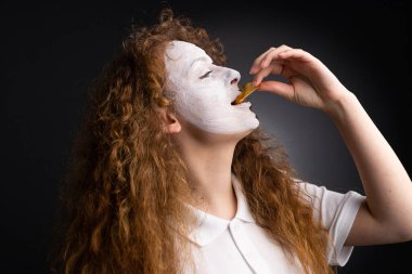 Beyaz tişörtlü fanatik bir kadının siyah arka planda yüz tatma cipsleriyle yan görüntüsü..