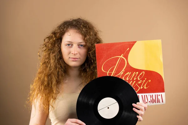 Selbstbewusste rothaarige Frau mit blauen Augen, die eine Vinylplatte mit klassischer Musik vor goldenem Hintergrund in den Händen hält. — Stockfoto