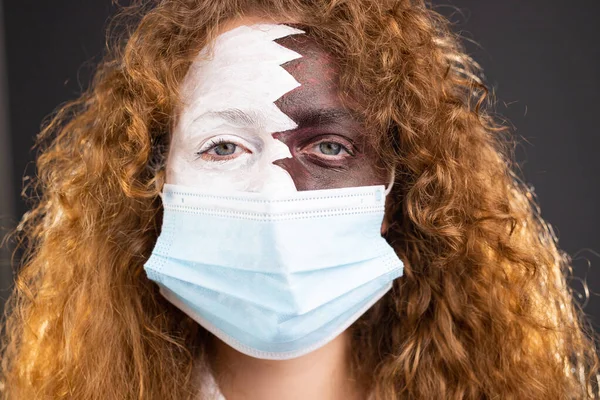 卡塔尔足球锦标赛上，一名红头发的球迷用医用口罩盖住了她的脸，脸上涂满了卡塔尔国旗. — 图库照片