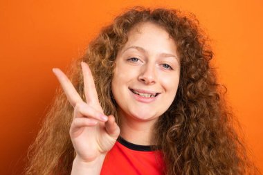 Mutlu kızıl saçlı, gülümseyen, güzel hayran futbolcu kadın iki parmağını portakal bahçesinde gösteriyor, futbol hayranı duyguları kavramı..