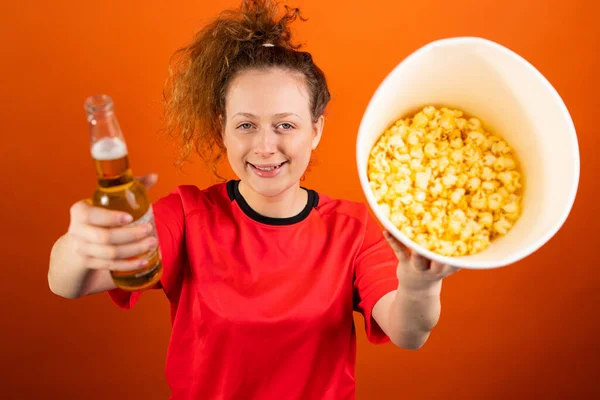 Glad kvinna fan fotboll tillbringa tid med att stödja sitt fotbollslag med en skål popcorn och en flaska öl. — Stockfoto