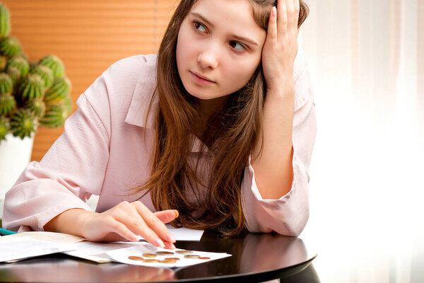 Молодая женщина, сидящая за столом, подсчитывая деньги для оплаты счетов, счетов и счетов.