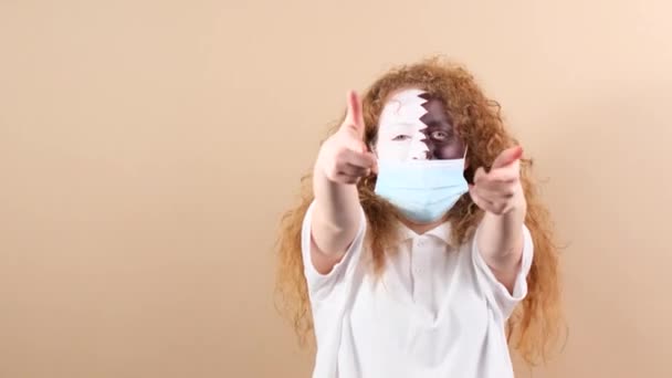 Tıbbi maskeli bir kadın Katar bayrağında yüzü boyalı sevinçle zıplıyor ve takımının zaferi olarak iki parmağını kaldırıyor.. — Stok video