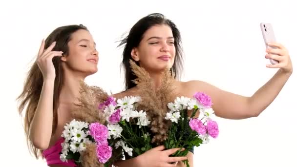 Két gyönyörű fiatal nő úgy néz ki, mint aki meztelenül elrejti a mellkasát csokor mögé, hogy szelfit csináljon okos telefonnal, tavaszi szépség koncepció. — Stock videók