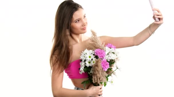 Gyönyörű szőke hölgy visel rózsaszín felső gazdaság a kezében csokor virág és a mobiltelefon, hogy szelfi. — Stock videók