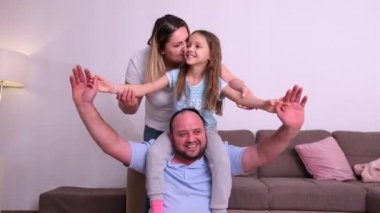 Mutlu bir aile hafta sonu evde vakit geçirir, kız babasının boynuna oturur ve uçak pozisyonu alır..