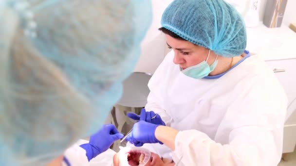 Медицинский персональный стоматолог ассистент в униформе лечит женские зубы пациентки, выполняющей хирургическую операцию. — стоковое видео