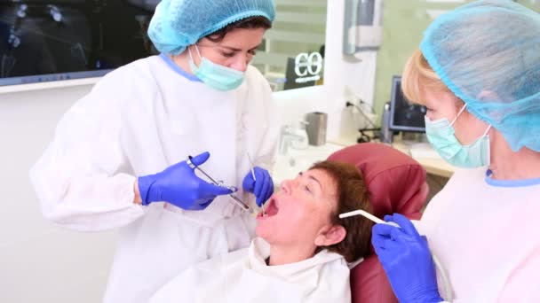 Fogorvosok és asszisztensek, akik a modern fogászati klinikán dolgoznak fogászati eszközökkel és injekciót adnak be a beteg rágójába. — Stock videók