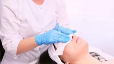 Mavi eldivenli kozmetolog spa salonunda tek kullanımlık kağıt peçete kullanarak kadın yüzündeki nemi temizliyor..