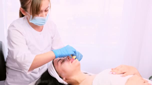 Kosmetolog v lékařské masce a modrých rukavicích se dvěma houbami odstraněnými z obličeje ženy omlazovací maska v salonu krásy. — Stock video