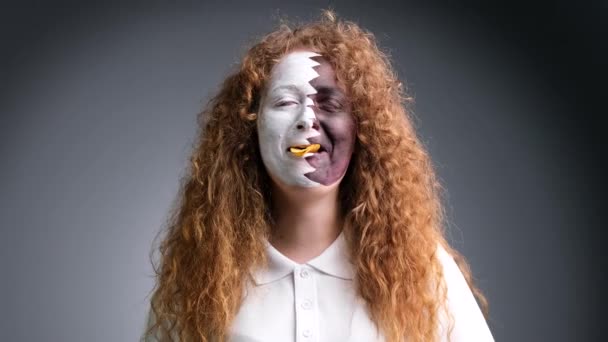 Redhead woman fan football with painted face in Qatar flag eating chips with very tasty expression over grey background. — Stock Video