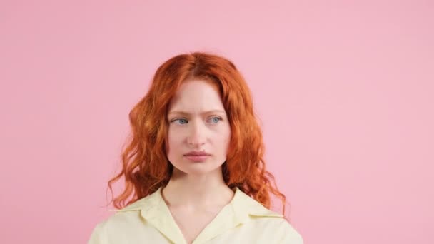Redhead wanita muda berdiri di depan kamera dan mengubah ekspresi wajahnya dari kesedihan menjadi kebahagiaan di latar belakang merah muda. — Stok Video
