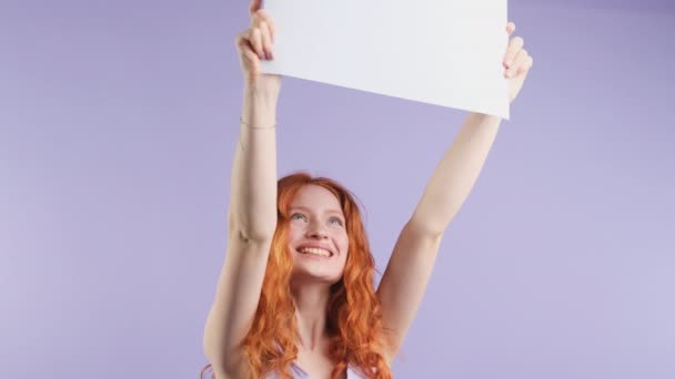Ενθουσιασμένος κατάπληκτος κοκκινομάλλα γυναίκα κρατώντας χαρτί με αντίγραφο χώρο για την υπηρεσία διαφημιστικού προϊόντος που απομονώνονται σε μωβ φόντο στούντιο. — Αρχείο Βίντεο