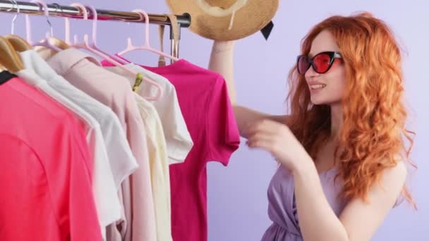 スタイルの赤毛の女性とサングラス頭の上に帽子をかぶって夏のための服を選ぶ、ショッピングの日のコンセプト. — ストック動画