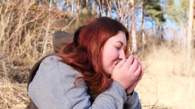 Sakinlik ve huzur dolu kızıl saçlı kadın elinde tuttuğu bardaktan sıcak bir içecekle ısınmaya çalışıyor..